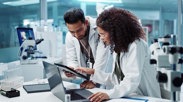 Two scientists collaborating in a lab using digital tools for drug discovery research. 