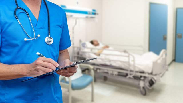 A doctor stands reviewing a patient’s chart on a hospital ward. 