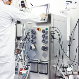 Scientist in protective suit operating a bioreactor system using a touchscreen in a cleanroom lab 