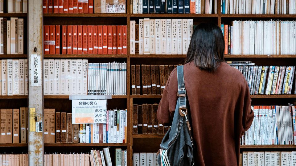 A person with long dark hair in a library, choosing books.