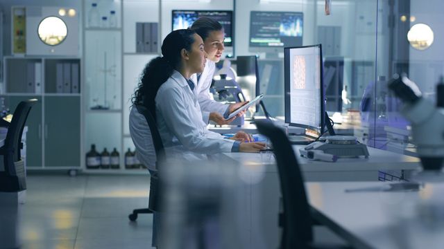 Two scientists analyzing data on a computer in a modern laboratory setting. 