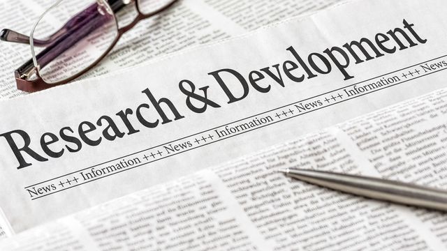 Newspaper titled "Research & Development", with a pen lying on top. 
