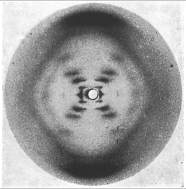 An XRD image of DNA showing a dark circle with a lighter ring inside and approximate cross shape with a clear hole at the center..